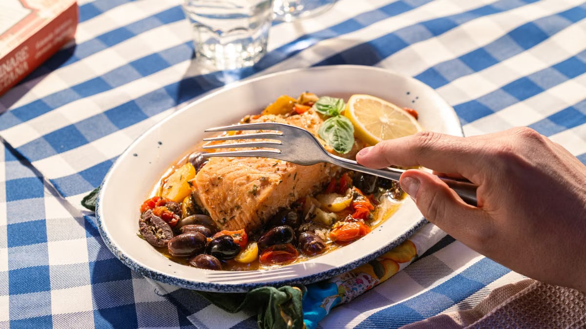 Delicious Mediterranean salmon with colorful vegetables on a blue checkered tablecloth.